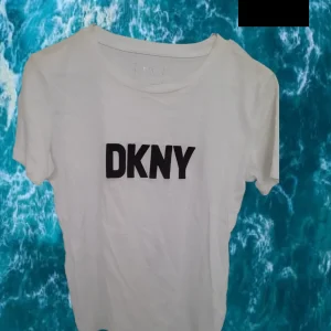 CAMISETA BLANCA MANGA CORTA CON LOGO DKNY BORDADO ( TARA DESCOLORIDO EN HOMBRO DERECHO )